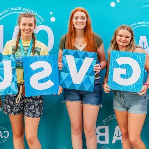 3 girls holding up "GVSU" letters in front of a CAB backdrop