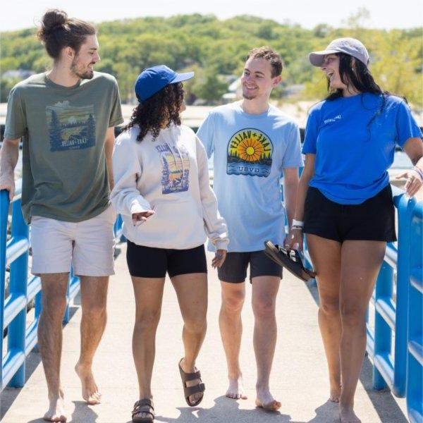 Four students wearing new Lake + Valley clothing items walk along the beach, laughing and talking together.